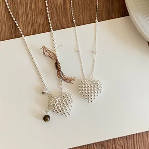 Close-up detail of textured 3D silver heart necklaces with bead charms on white card.