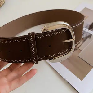 Close-up detail of a vintage brown wide belt with silver buckle and white zigzag stitching.