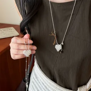 Close-up of a silver beaded heart pendant necklace displayed on a dark brown sweater.