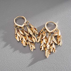 Close-up of elegant gold metallic wheat leaf tassel drop earrings on grey leather texture