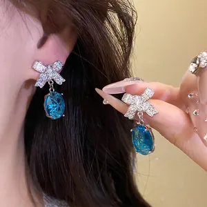 Élégantes boucles d'oreilles nœud argentées avec grands cristaux bleus ovales et zircons.