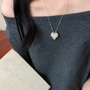 Close-up detail of a silver beaded heart necklace on a model wearing grey top