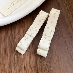 Detail of two beige fabric floral bow hair clips on a rustic wooden background