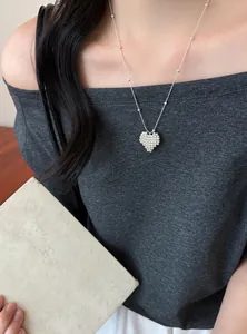 Detail view of a silver 3D beaded heart necklace on a model wearing an off-shoulder grey top