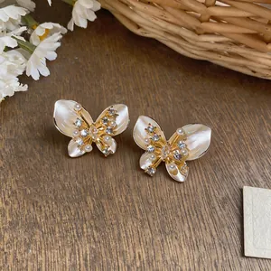 Detailed close-up of dainty gold butterfly earrings with pearl and crystal inlay