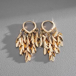 Detail shot of vintage style gold metallic leaf tassel hoop earrings on grey leather.