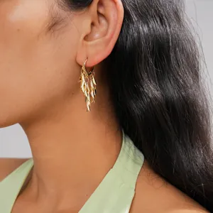 Close-up detail of gold leaf tassel earrings worn by a model in a light green top