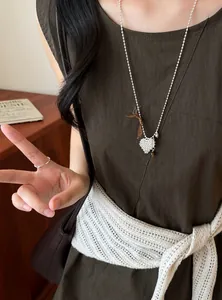 Close-up view of a silver-colored textured heart pendant sweater necklace on a model