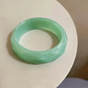 Close-up of a light green faceted acrylic bangle with marbled resin texture