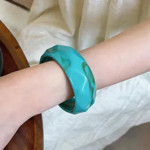 Detail view of a vintage-style turquoise faceted acrylic bangle worn on a model's wrist
