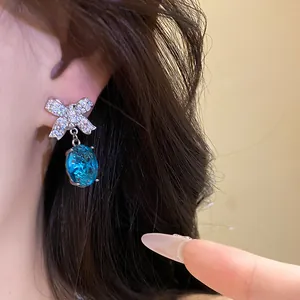 Gros plan d'une boucle d'oreille nœud avec zircons et une pierre goutte bleue ovale.
