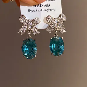 Détail des boucles d'oreilles nœud scintillant avec pendentif cristal bleu ovale.