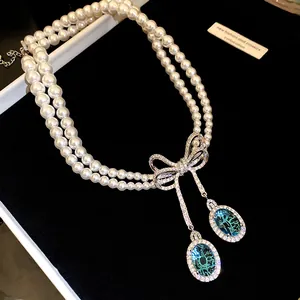 Gros plan d'un collier de perles double rang avec un nœud en zircon et pierres bleues.