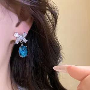 Gros plan de boucles d'oreilles nœud en cristal bleu élégantes avec zircons sur l'oreille.