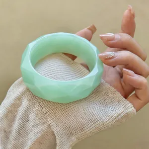 Close-up of a faceted light green acrylic bangle worn on a wrist over a knit sleeve.