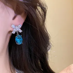 Détail d'une boucle d'oreille en cristal bleu avec un nœud étincelant sur l'oreille.