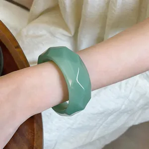 Close-up view of a retro faceted green acrylic bangle on a woman's wrist.