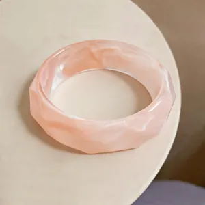 Macro detail of faceted acrylic bangle with peachy marble texture and high-gloss finish