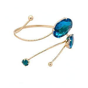 Elegant gold spiral arm cuff with large oval blue crystal stones, minimalist style.
