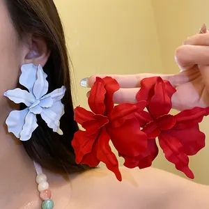 Close-up detail of oversized floral stud earrings in matte red and white finishes