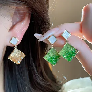 Nahaufnahme von 14k vergoldeten geometrischen Diamant-Ohrhängern mit grünem und gelbem Glas.