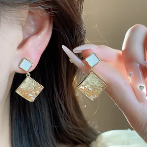 Nahaufnahme von 14 Karat vergoldeten geometrischen Ohrringen mit bernsteinfarbenem Glas.