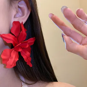 Close-up detail of a large red matte spray-painted flower earring on a female model's ear.