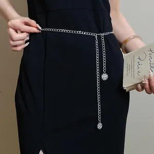 Close-up of minimalist silver chain belt detail with hanging circular charms on black dress