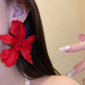 Close-up of a large matte red flower stud earring worn on a model's ear
