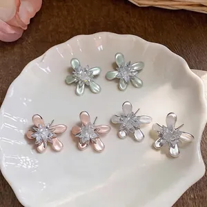Elegant flower stud earrings with pearlescent petals and crystal centers on a shell plate