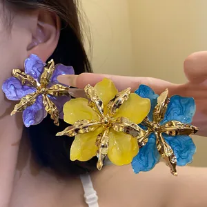 Gros plan de grandes boucles d'oreilles fleurs froissées en jaune, bleu et violet vifs.