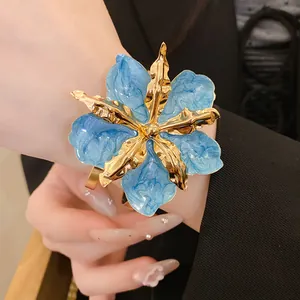 Gros plan détaillé montrant une grande boucle d'oreille fleur en émail bleu et doré