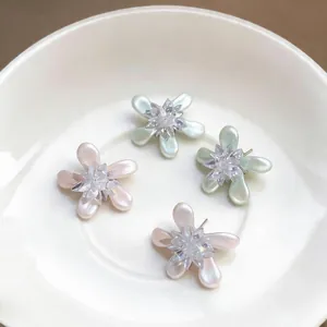 Close-up of elegant floral stud earrings with pearlescent petals and crystal centers.