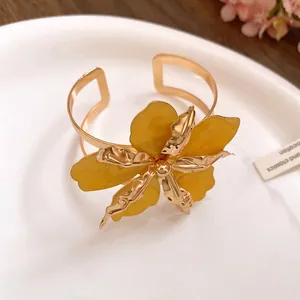 Gros plan d'un bracelet manchette doré avec fleur jaune et pétales plissés élégants.