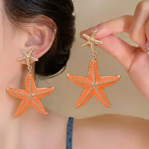 Close-up of elegant orange enamel starfish earrings with gold textured finish details