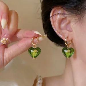 Élégantes boucles d'oreilles en verre vert en forme de cœur portées par un mannequin
