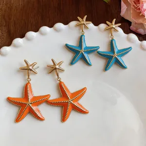 Detailed view of vibrant orange and blue enamel starfish earrings on a decorative white plate