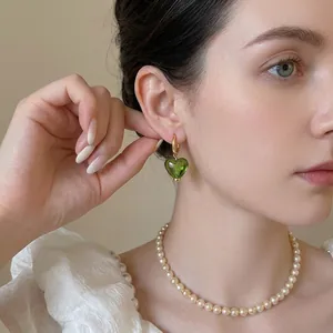 Élégantes boucles d'oreilles créoles dorées 24 carats avec cœur vert sur un mannequin
