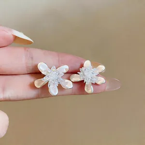 Detailed view of elegant white glass flower stud earrings held to show delicate size