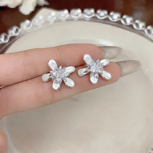 Detailed macro view of silver flower stud earrings with white petals and crystal center