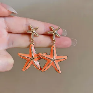 Close-up of orange enamel starfish drop earrings in gold-tone finish