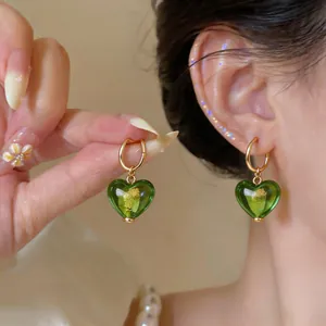 Détail de boucles d'oreilles plaquées or 24 carats avec cœurs verts et feuilles d'or