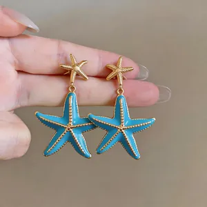 Close-up detail of bright blue enamel starfish drop earrings with elegant golden trim finish
