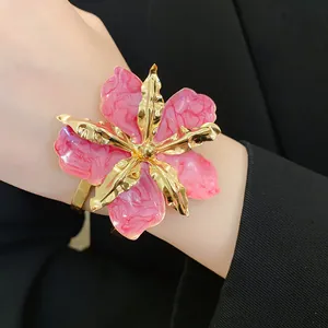 Gros plan d'un bracelet manchette en émail rose avec des bords dorés sur un poignet.