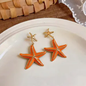 Detailed macro shot of orange enamel starfish drop earrings with gold-tone accents