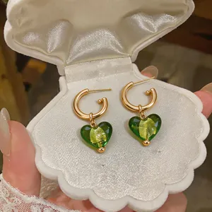 Gros plan de boucles d'oreilles plaquées or 24 carats avec pendentifs cœurs verts en verre.