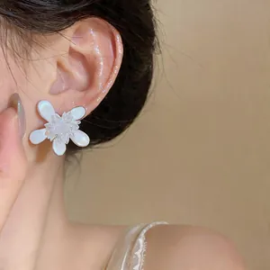 Close-up detail of white glass flower stud earrings worn on ear for minimalist style