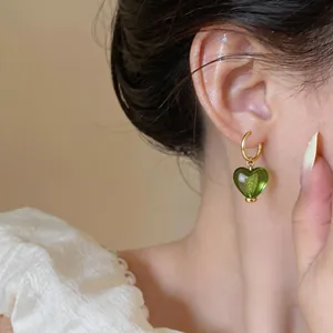 Détail de boucles d'oreilles créoles cœur vert avec placage or 24 carats sur l'oreille