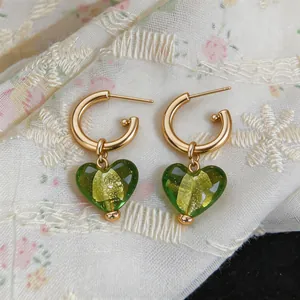 Détail de créoles dorées avec des pendentifs en verre en forme de cœur vert et feuille d'or