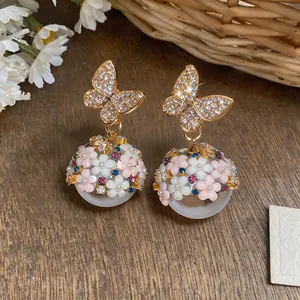 Dettaglio di eleganti orecchini a farfalla dorati con sfere floreali e cristalli colorati.